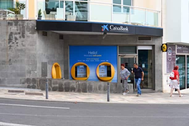 People outside CaixaBank ATM reflecting banking in trade and Incoterms payments