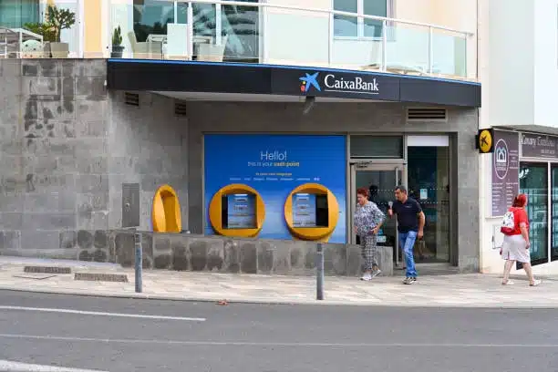 People outside CaixaBank ATM reflecting banking in trade and Incoterms payments