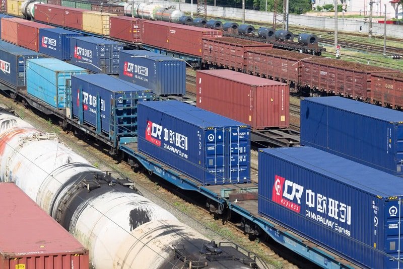 Flatbed trains loaded with blue and red China Railway Express cargo containers at a rail yard