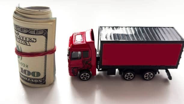 Red cargo truck beside rolled US dollars representing shipping and freight costs