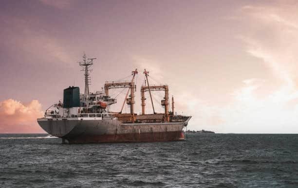 Cargo ship sailing in the ocean during sunset, transporting bulk freight