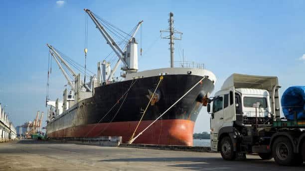 Cargo ship docked with truck beside it, representing multimodal transport for heavy goods