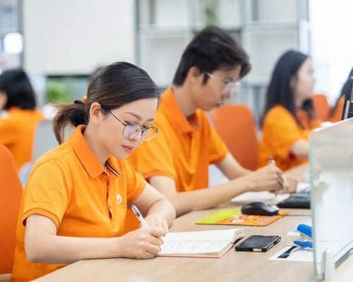 GWT logistics staff in orange uniforms working at desks, writing notes and using computers in the office
