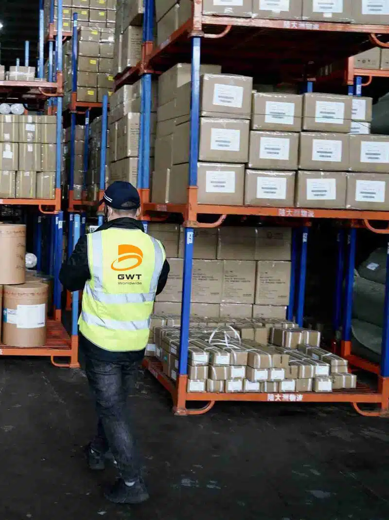 GWT employee in high-visibility vest inspecting palletized boxes on warehouse racks