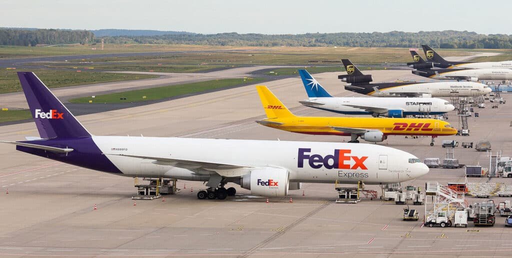 FedEx, DHL, UPS, and other express cargo aircraft lined up at an airport apron ready for loading