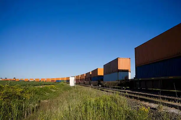 Freight containers on train moving through countryside under blue sky
