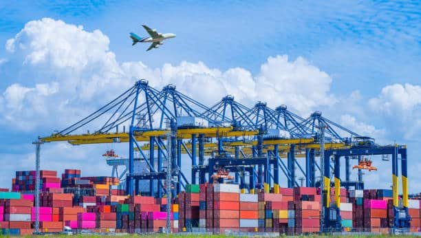 Un port avec plusieurs grues et des conteneurs colorés empilés, ainsi qu'un avion cargo survolant le port, illustrant la logistique portuaire.