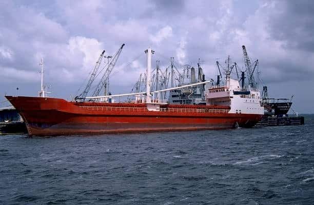 Large red ship docked at port, loading shipping containers for transport