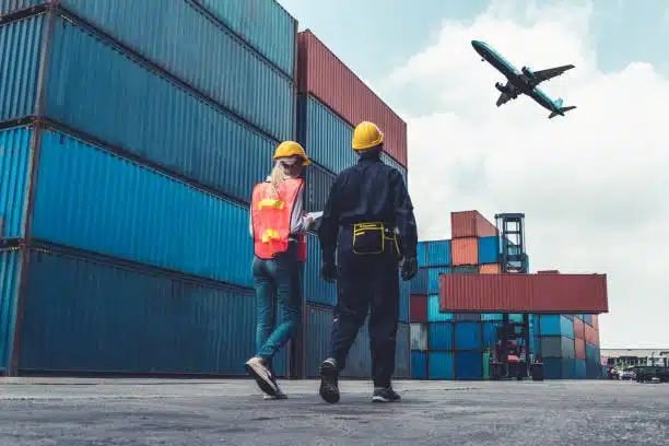Two logistics workers inspecting containers with airplane flying above