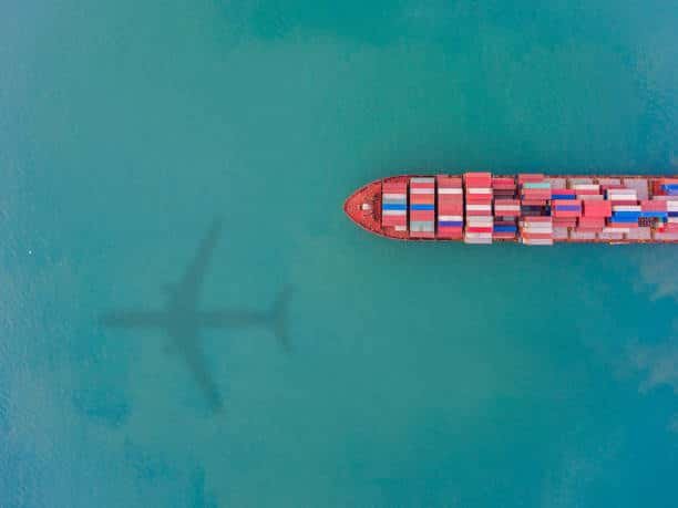 Aerial view of container ship with airplane shadow above, illustrating multimodal freight