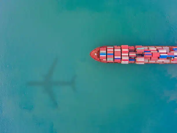 Aerial view of container ship with airplane shadow above, illustrating multimodal freight
