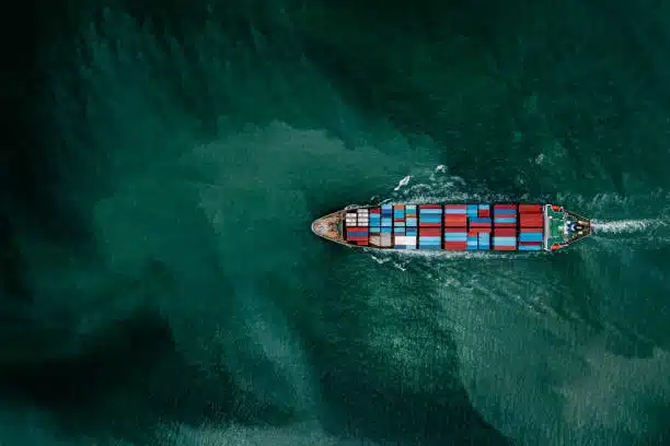 Top-down view of a container ship sailing through green ocean waters, representing international ocean freight logistics