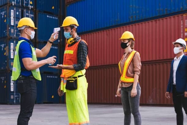 Air freight logistics workers undergoing temperature check and sanitization during cargo handling at container yard