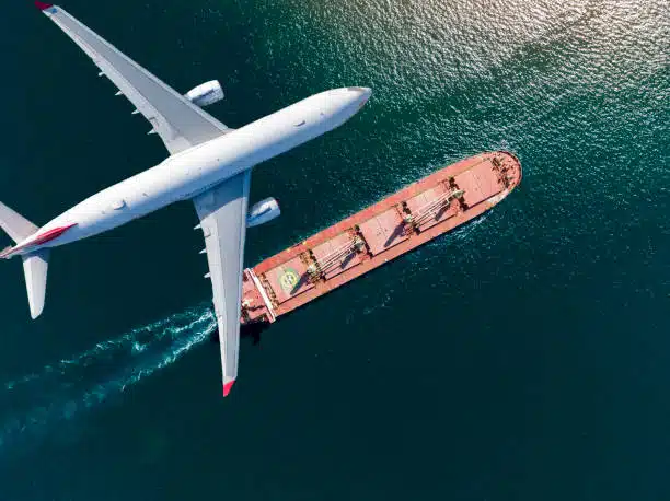 Aerial view of airplane flying over cargo vessel, depicting combined air and ocean freight