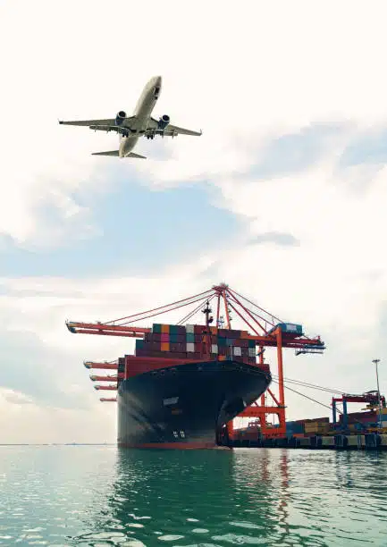 Airplane taking off above a container ship docked at port, illustrating dual transport modes