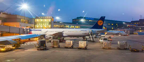 Airport cargo terminal showing containers being loaded on Lufthansa aircraft.