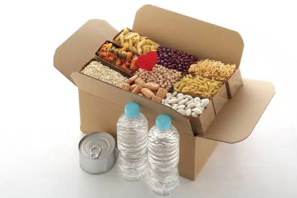 A variety of dried foods like pasta, beans, and grains packaged for delivery with water bottles and canned food.