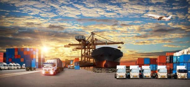 Portside operation with drayage trucks, container stacks, and ship under crane, illustrating high-volume intermodal logistics.