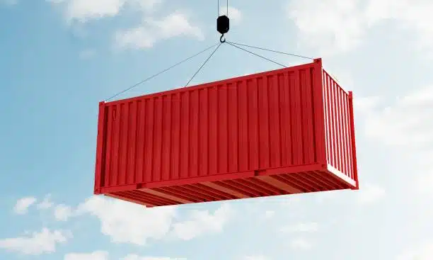 Red shipping container lifted by crane for international freight