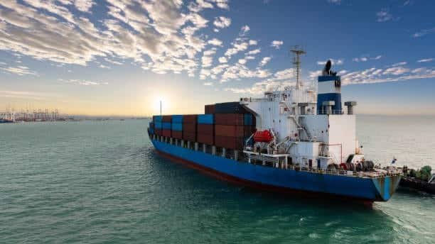 Cargo ship carrying freight containers arriving at port as part of the intermodal supply chain linked to drayage trucking.