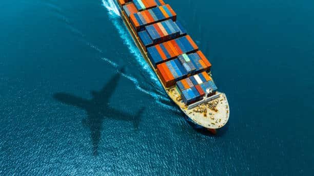 Colorful containers on cargo ship with aircraft shadow over the ocean – sea and air freight from China to Sweden