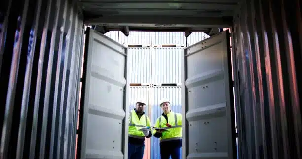 Two logistics workers reviewing cargo shipment inside an open container