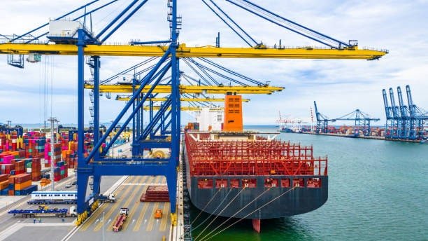 Container ship moored at a calm bay in Singapore, being serviced by terminal cranes