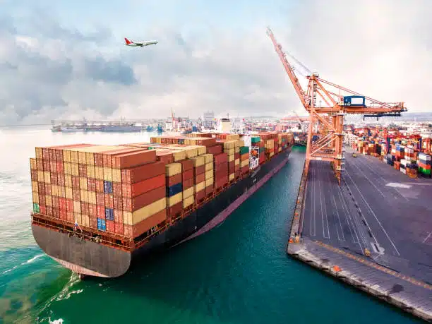 Loaded container ship departing port with an airplane in the sky, headed for Bangladesh