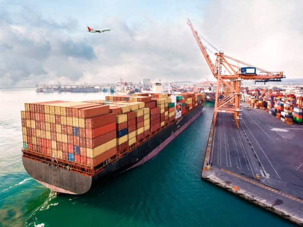 Loaded container ship departing port with airplane overhead, heading toward Venezuela