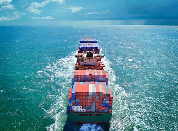 Rear view of a container ship navigating international ocean freight shipping routes with stacked cargo at sea