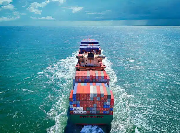 Rear view of a container ship navigating international ocean freight shipping routes with stacked cargo at sea