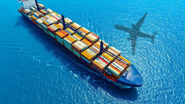 Aerial view of a cargo ship at sea with shadow of an airplane, depicting combined shipping methods from China to Saudi Arabia.