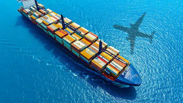 Aerial view of a cargo ship at sea with shadow of an airplane, depicting combined shipping methods from China to Saudi Arabia.