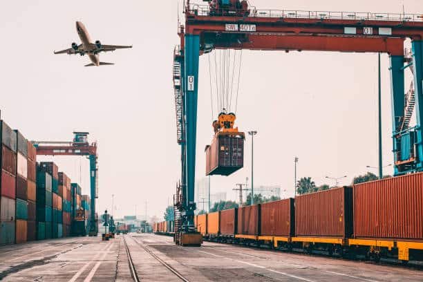 Logistics crane lifting container at terminal with airplane overhead, symbolizing air and rail freight to UK