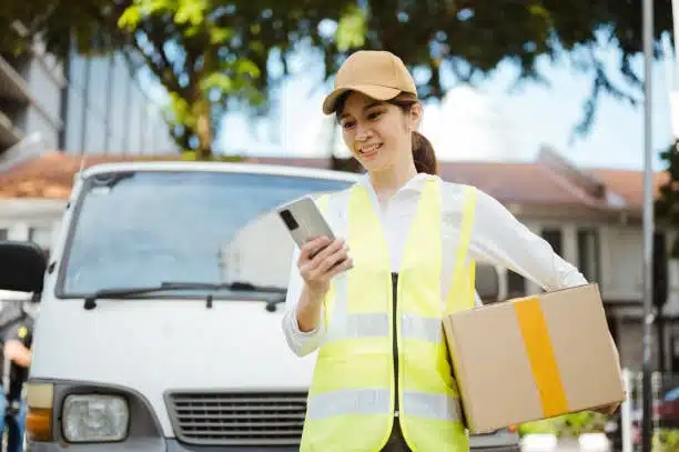 Smiling delivery woman holding a parcel and using a smartphone for updates