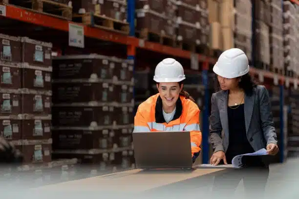 Female workers in safety gear reviewing export documents on a laptop