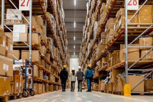 Large warehouse aisle with stacked boxes and workers inspecting inventory for dropshipping logistics