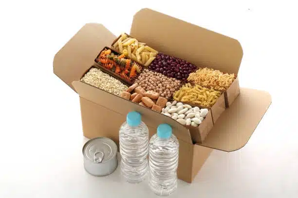 Cardboard box filled with assorted dry perishable food items, beans, pasta, and water bottles ready for shipping.