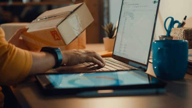 Person entering shipment data on laptop while holding a parcel box