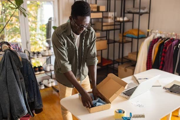 Entrepreneur packaging clothing items in a home office for dropshipping delivery