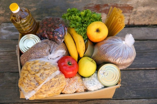 Food package combining fresh produce like bananas and tomatoes with dry food and canned goods for perishable shipping.