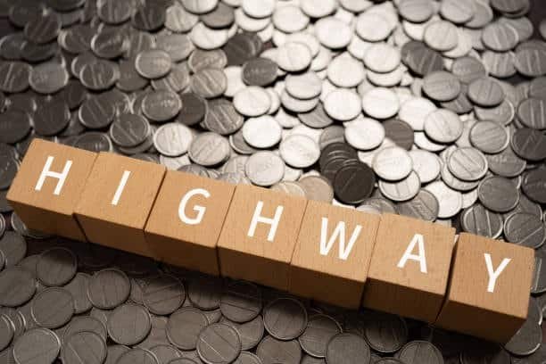 Wooden blocks spelling highway on coins representing toll costs in logistics