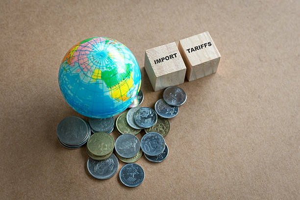 Globe, coins, and wooden blocks labeled import tariffs symbolizing international trade charges