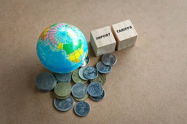 Globe, coins, and wooden blocks labeled import tariffs symbolizing international trade charges