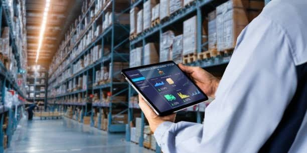 Logistics manager monitoring import data in a warehouse with shelves of goods