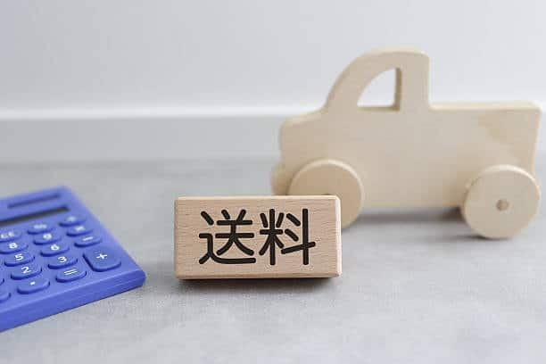 Wooden block with Japanese kanji for shipping cost, calculator and toy vehicle