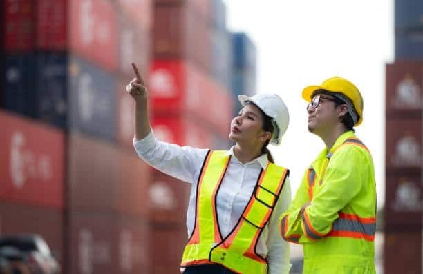 Two logistics supervisors inspecting container stacks at a shipping terminal