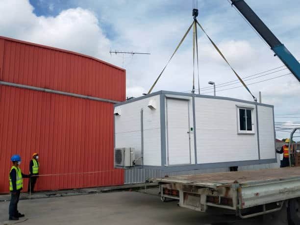 Crane loading a prefabricated structure onto a trailer for international shipping