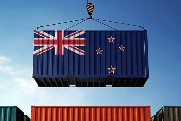 Large cargo container with New Zealand flag being hoisted at global shipping port
