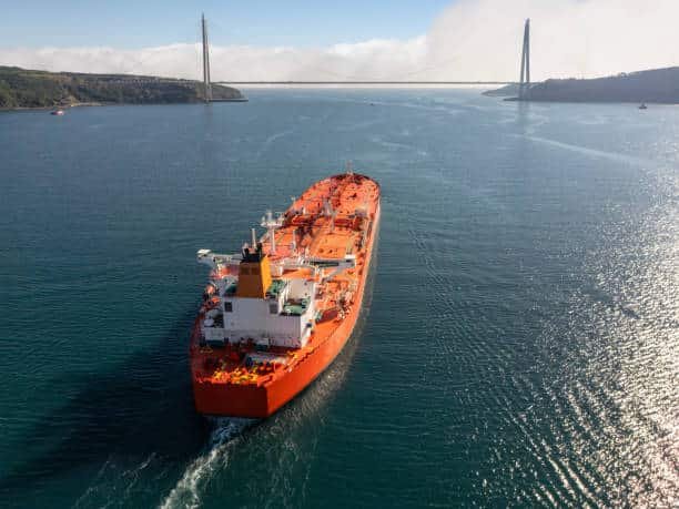 Large tanker ship navigating through a wide waterway under a bridge